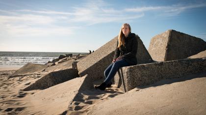 Elles zit in een dikke jas op het strand in het zonnetje