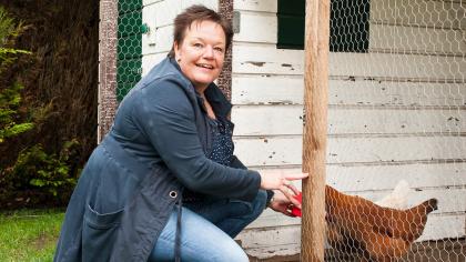 Jannie zit op haar hurken en voert de kippen in het kippenhok.