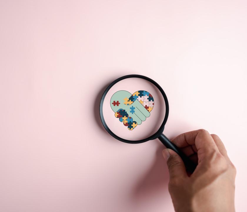 Vergrootglas op handen die een hartje vormen met puzzelstukjes